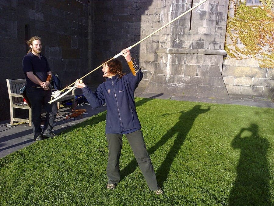 A person's arm drawn back, holding an atlatl with a long dart seated on its spur, ready to throw.