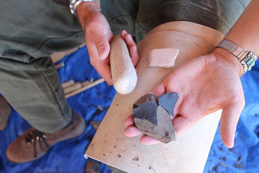 Close view of a demonstrator's hands striking flakes from a stone core during a flintknapping demonstration at a national monument.